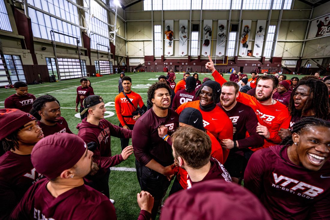 Benjamin Eziuka in the middle of a team huddle celebration inside the Virginia Tech indoor practice facility.