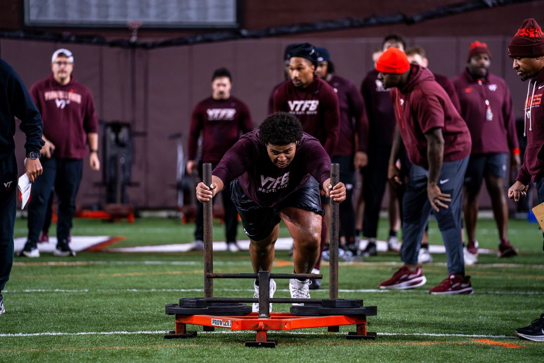 Benjamin Eziuka driving a weighted sled across the turf during a Virginia Tech conditioning session.
