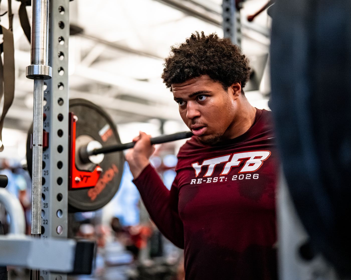 Benjamin Eziuka under a squat bar in a Virginia Tech football shirt, focused, in the weight room.