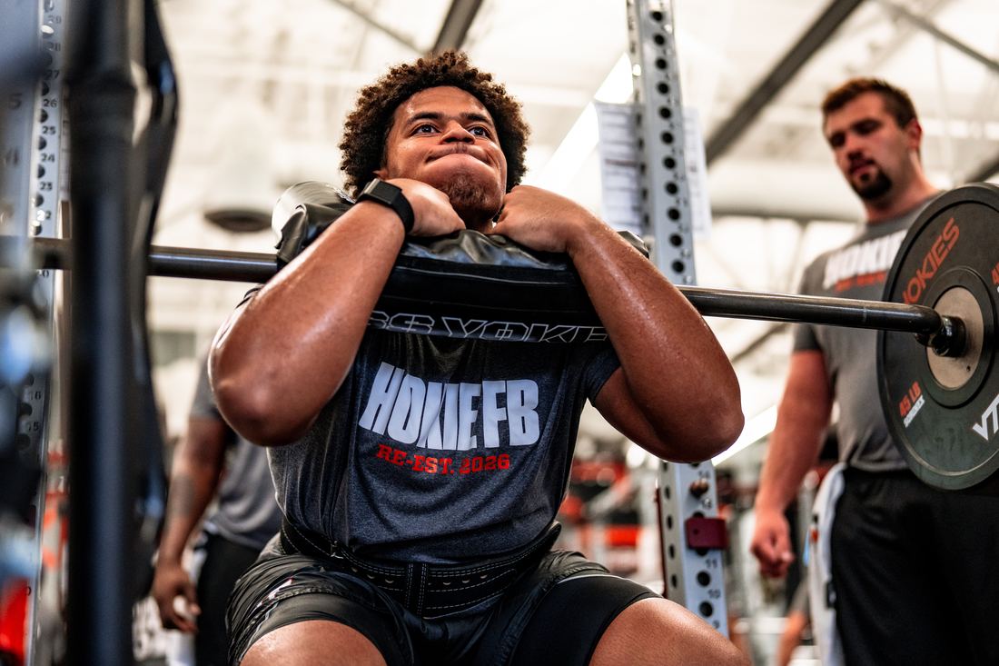 Benjamin Eziuka squatting a weighted bag in the Virginia Tech training facility.