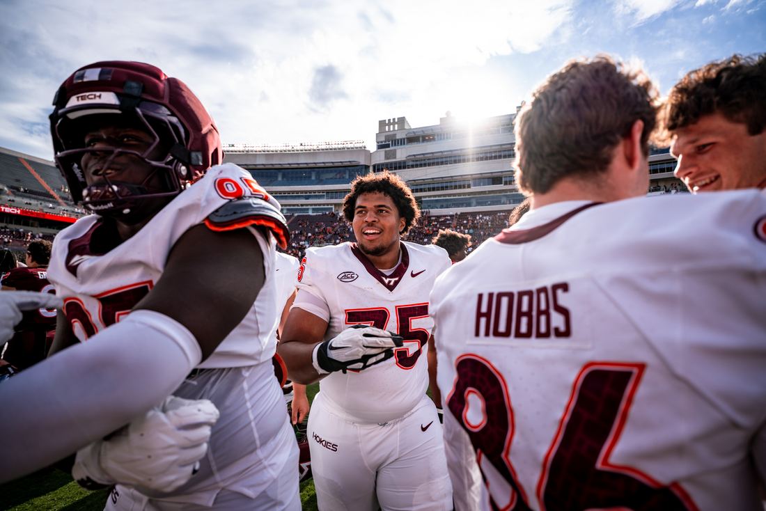 Benjamin Eziuka smiling in his number 75 game jersey among teammates on the field after a game, one teammate’s jersey reading Hobbs.
