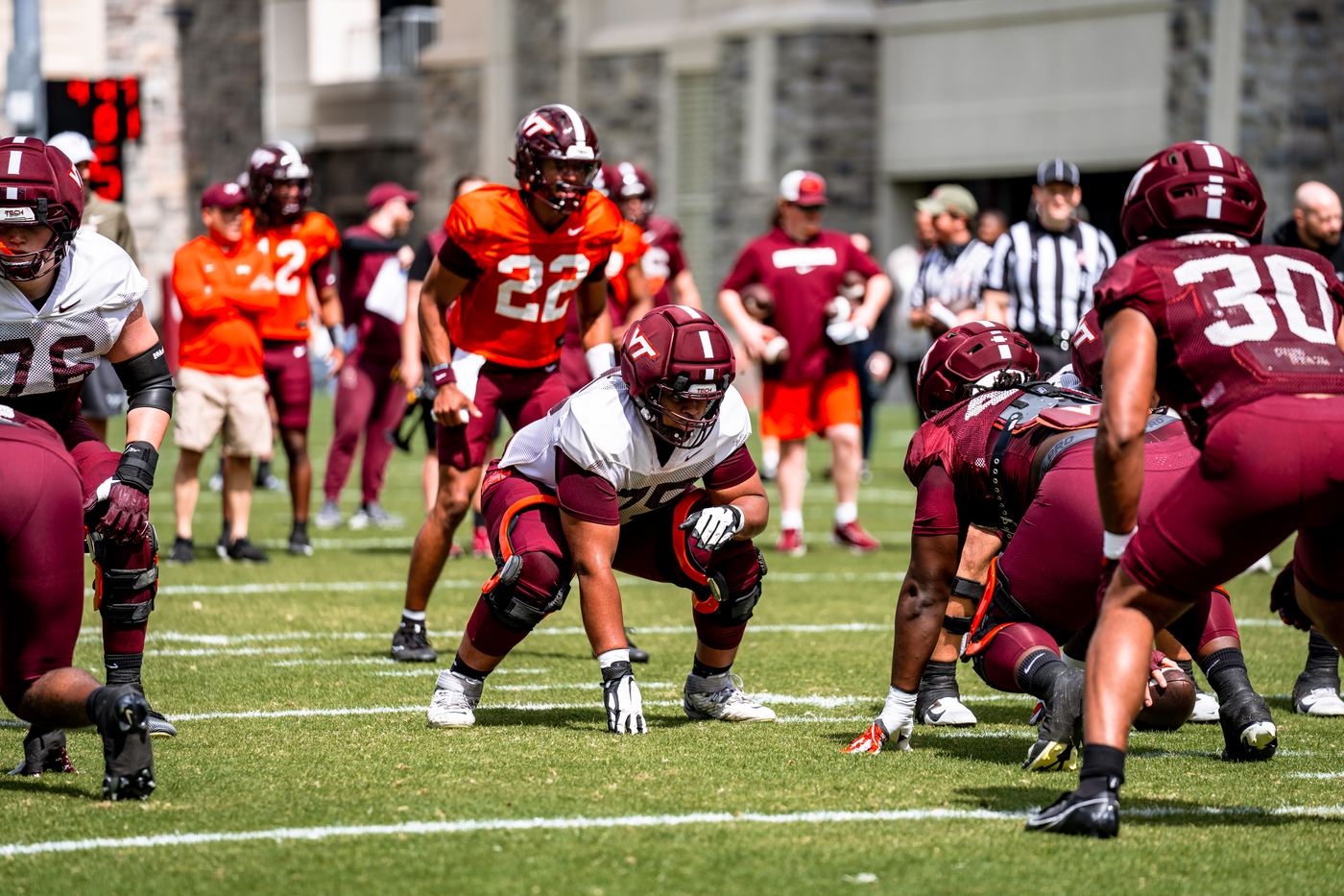 Benjamin Eziuka in a stance at the line of scrimmage during a Virginia Tech practice, teammates and coaches in the background.