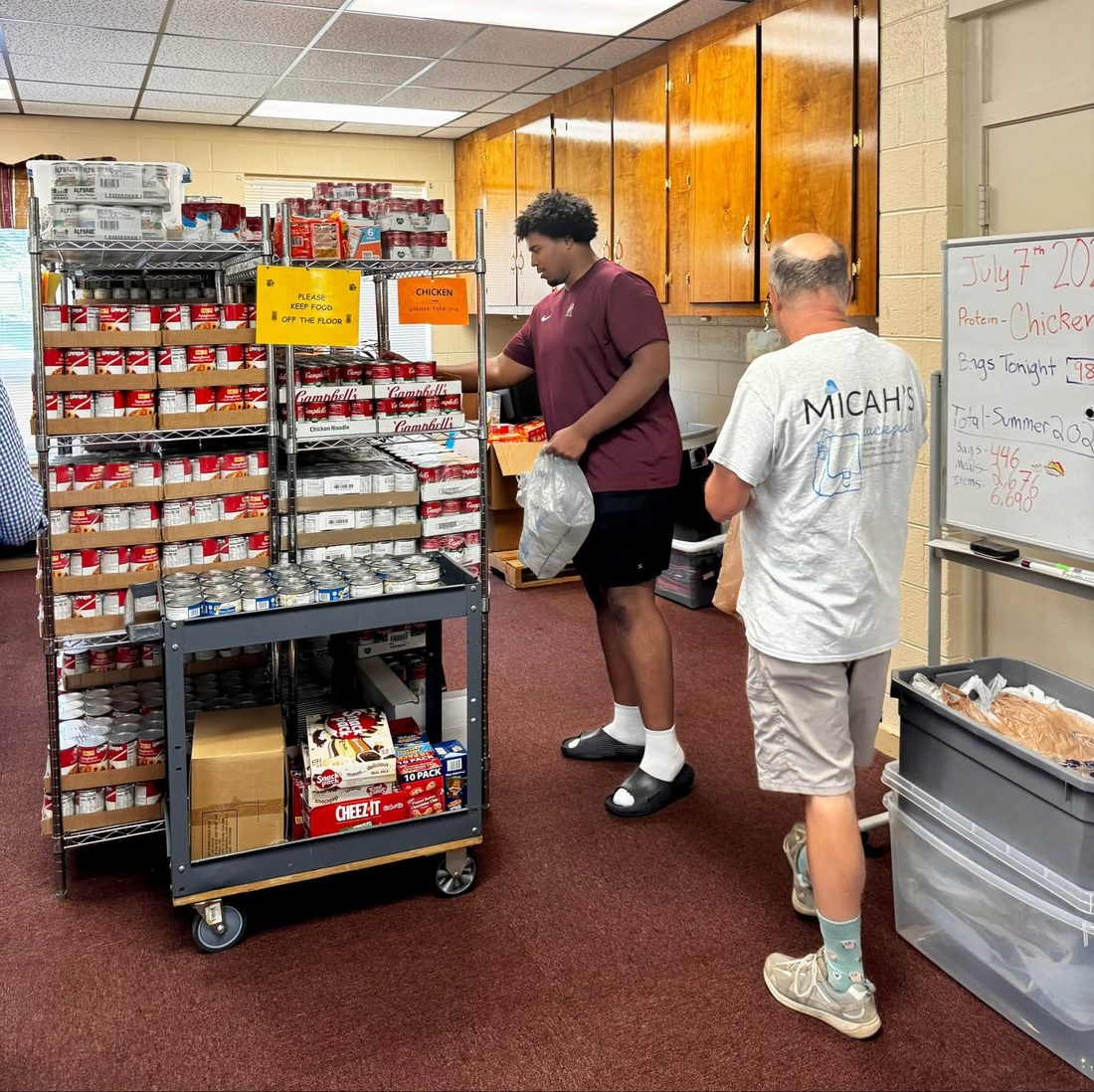 Benjamin Eziuka stocking canned food on shelves alongside a Micah's Backpack volunteer at a Blacksburg food pantry.