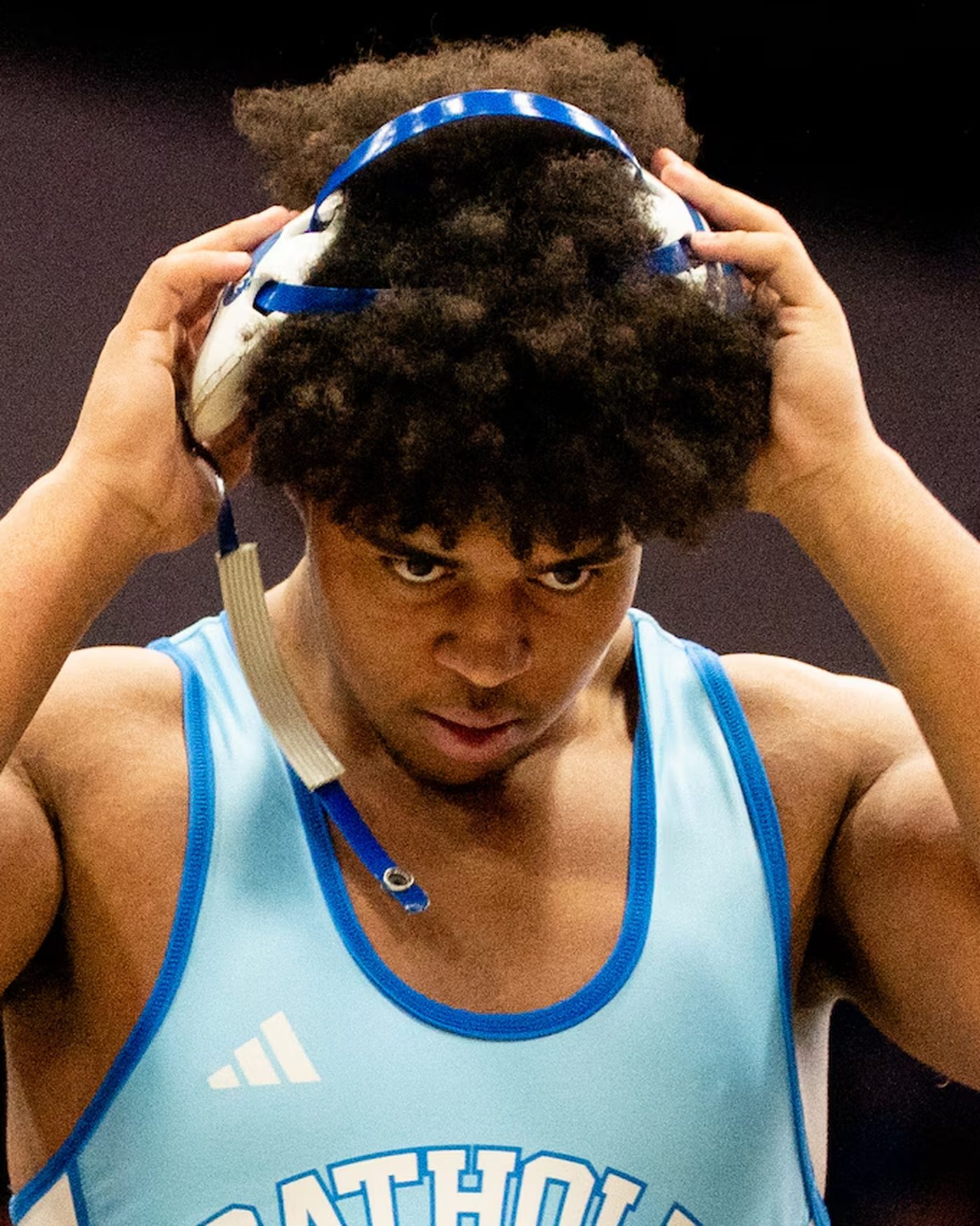Benjamin Eziuka adjusting his headgear in a Detroit Catholic Central wrestling singlet.